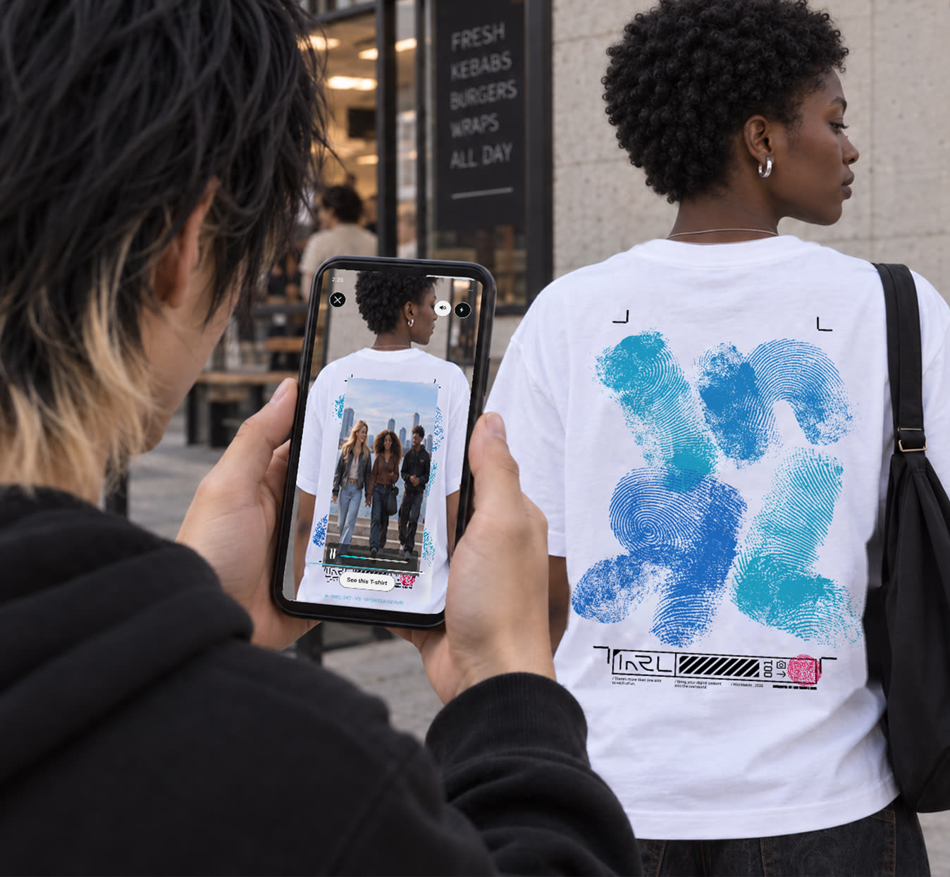 Someone films the print on an INRL T-shirt with their phone, and the video plays on screen.